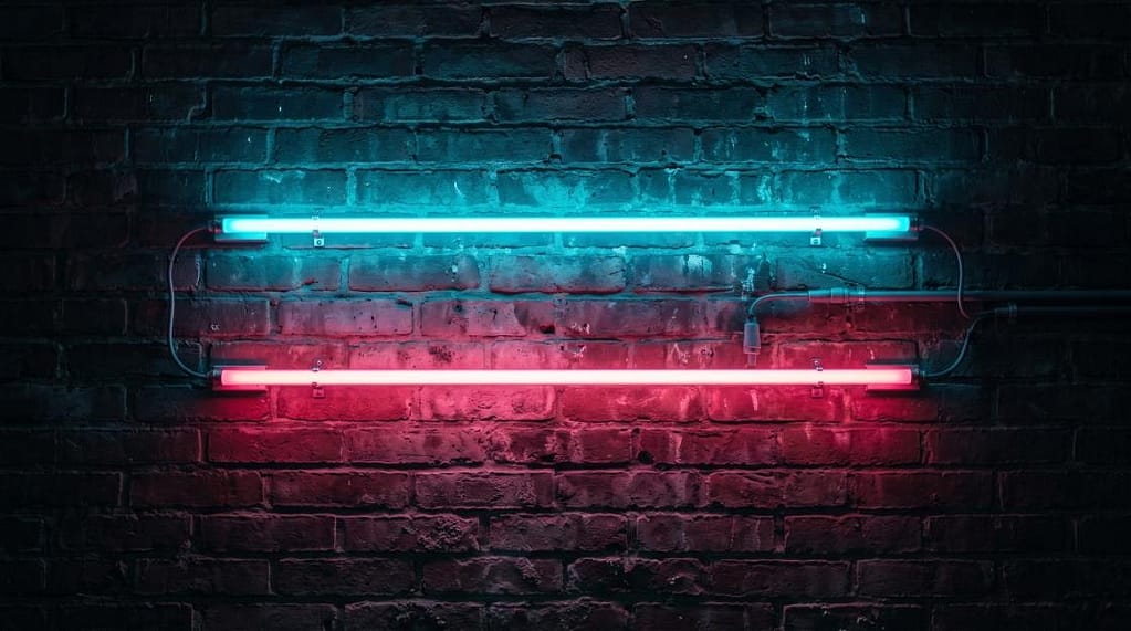 Cyan blue and pink neon light tubes glowing on a dark brick wall texture